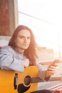 Portrait of young man playing guitar while holding smart phone