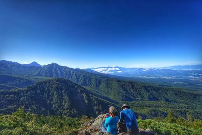 Rear view of friends standing on mountain against clear blue sky