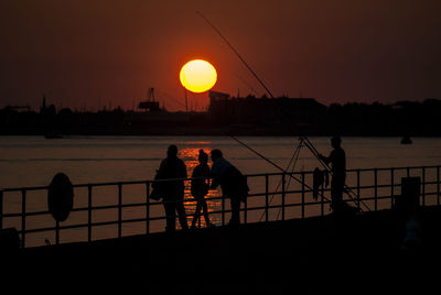 Silhouette people standing by railing on pier against sky during sunset