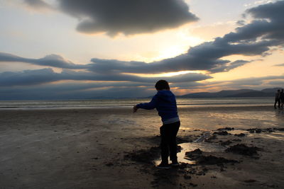 Full length of man standing on beach against sky during sunset