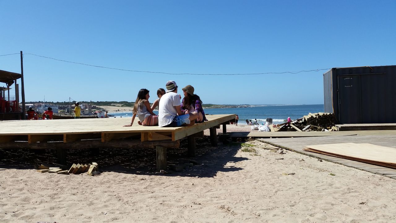 beach, sea, clear sky, sand, horizon over water, water, shore, copy space, lifestyles, person, leisure activity, men, large group of people, vacations, sky, sunlight, blue, day, incidental people