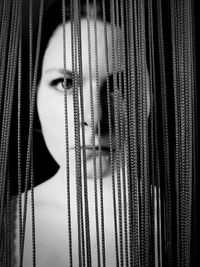 Close-up portrait of woman standing behind strings against black background