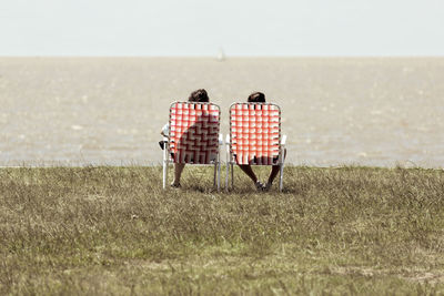 Rear view of people sitting on chair at beach