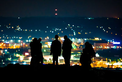 Silhouette people standing in illuminated city against sky at night