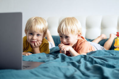 Cute kids lying on bed while looking at laptop