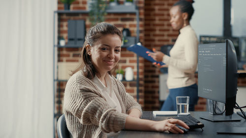 Portrait of smiling young woman using mobile phone while sitting in office