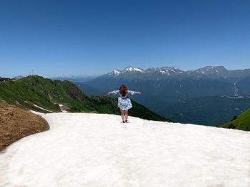 Rear view of woman standing on snow against mountain and sky