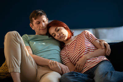Couple in love sitting on couch and hold hands, embracing in own apartment. emotional connection
