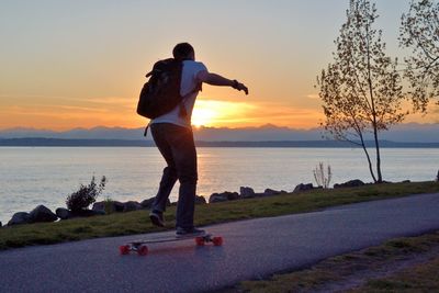 Rear view of man skateboarding on street by lake