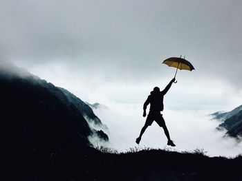 Excited silhouette man jumping with umbrella against foggy weather