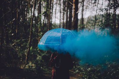 Woman with umbrella and blue smoke standing in forest
