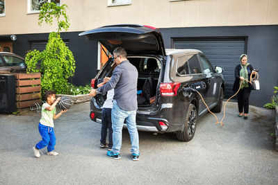 Father playing with children while mother rolling electric charger by car