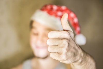 Close-up of man in santa hat showing thumbs up at home