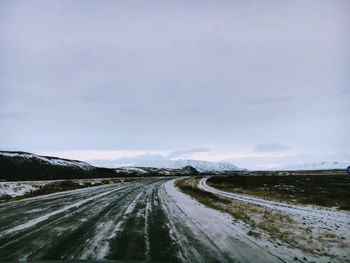 Road amidst snow covered landscape against sky