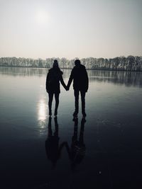 Silhouette couple holding hands while standing on ice rink against sky