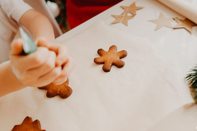 A child squeezes food dye from a tube onto a finished gingerbread cookie on a white table