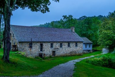 Old house on field by trees against sky