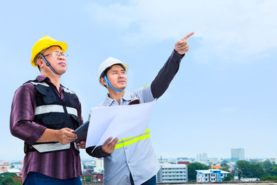 Young man with arms raised standing against sky