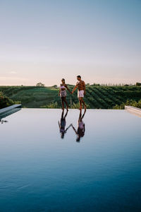 Full length of couple standing by swimming pool against sky