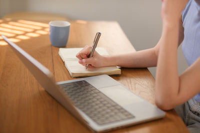 Midsection of woman using laptop at table