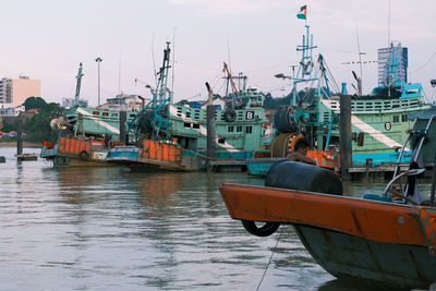 Fishing boats moored at harbor against sky