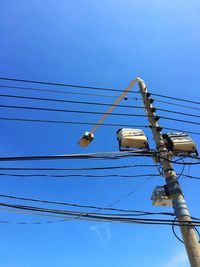 Low angle view of street light with electricity cables against blue sky