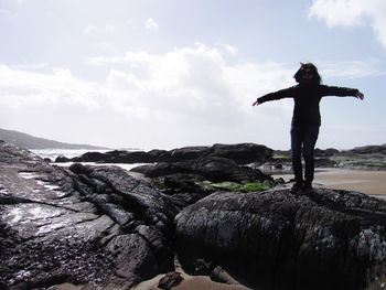 Man standing on cliff by sea against sky