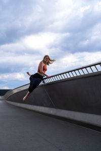 Low angle view of woman climbing on bridge against sky