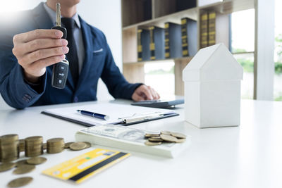 Midsection of businessman holding key with currency at desk