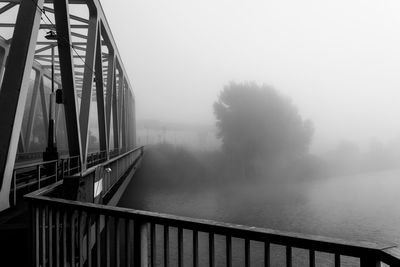 Bridge by trees against sky during foggy weather