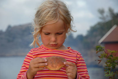 Close-up of girl holding food while standing outdoors against sky