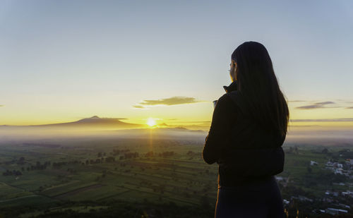 Rear view of woman standing against sky during sunset