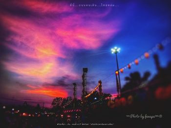 Low angle view of illuminated factory against sky at sunset