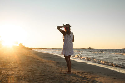 Young woman just graduated walking on the beach at sunset with laurel wreath
