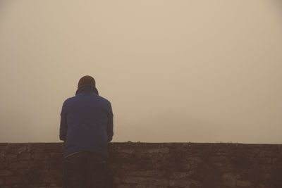 Rear view of man standing by retaining wall during foggy weather