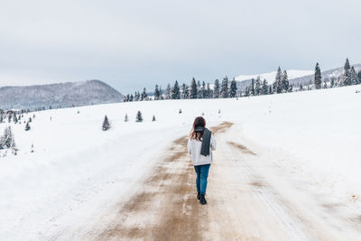 Rear view of man walking on snow covered landscape