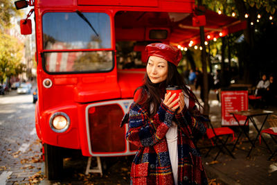 Beautiful asian woman in plaid coat and red leather hat on street with coffee