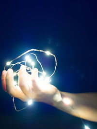 Low angle view of hand against illuminated blue sky