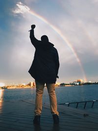 Rear view of man standing on jetty at beach against sky