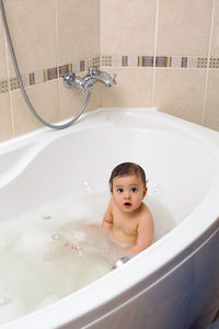 Baby boy sitting in bath with water and foam