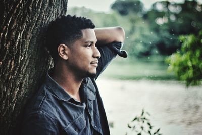 Man looking away against tree trunk