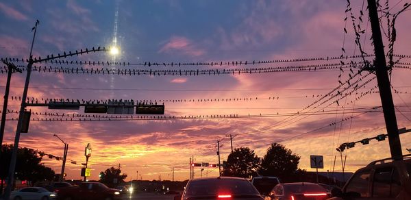 Cars on street against sky at sunset