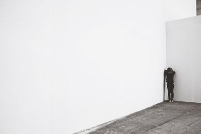 Rear view of girl leaning on white wall while playing hide and seek