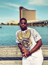 Portrait of young man wearing sunglasses standing against river