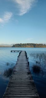 Wooden pier over lake against clear blue sky on sunny day. 