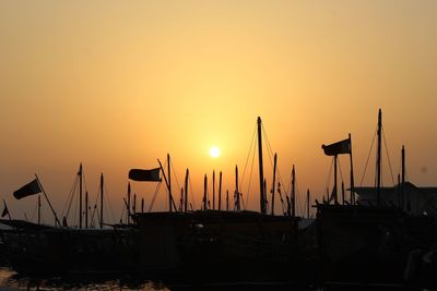 Silhouette sailboats moored at harbor against sky during sunset