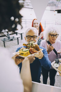 Owner giving food to male senior customer in city