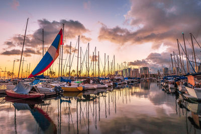 Sailboats moored on sea against cloudy sky during sunset