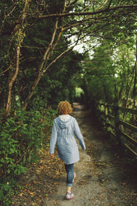 Full length rear view of woman walking on pathway amidst trees