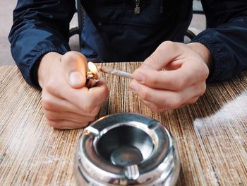 Midsection of man lighting cigarette at wooden table